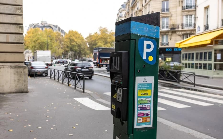 Rue parisienne haussmannienne avec horodateur au premier plan et voitures garées le long du trottoir